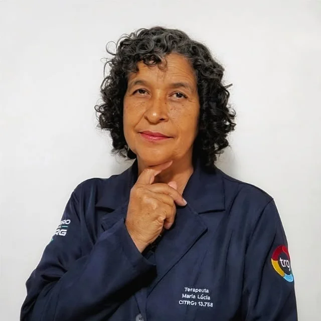 Maria Lúcia, de cabelos cacheados e blazer azul, com a mão apoiada no queixo.